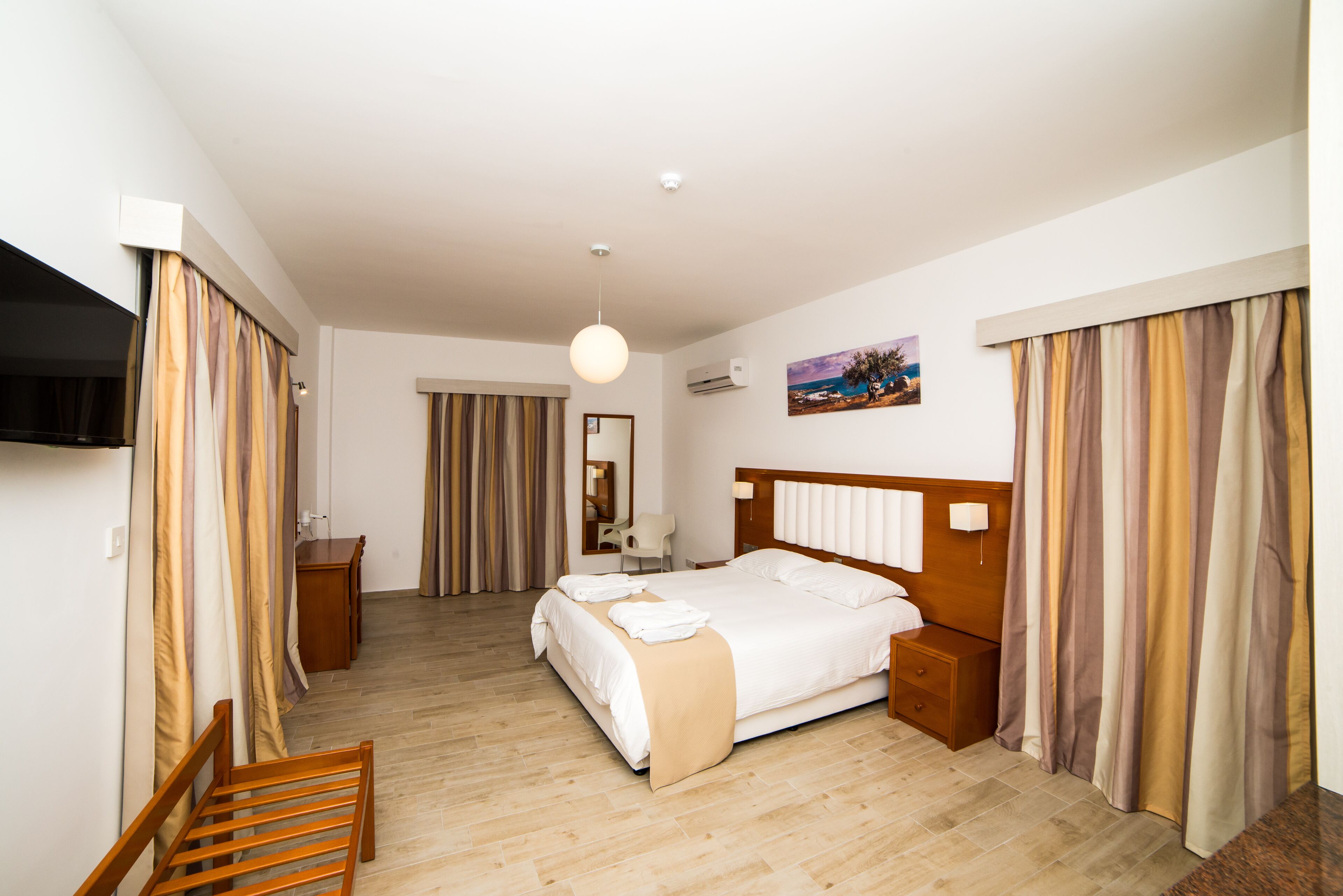 A hotel room with a bed, bedside table, chair, and a painting on the wall.