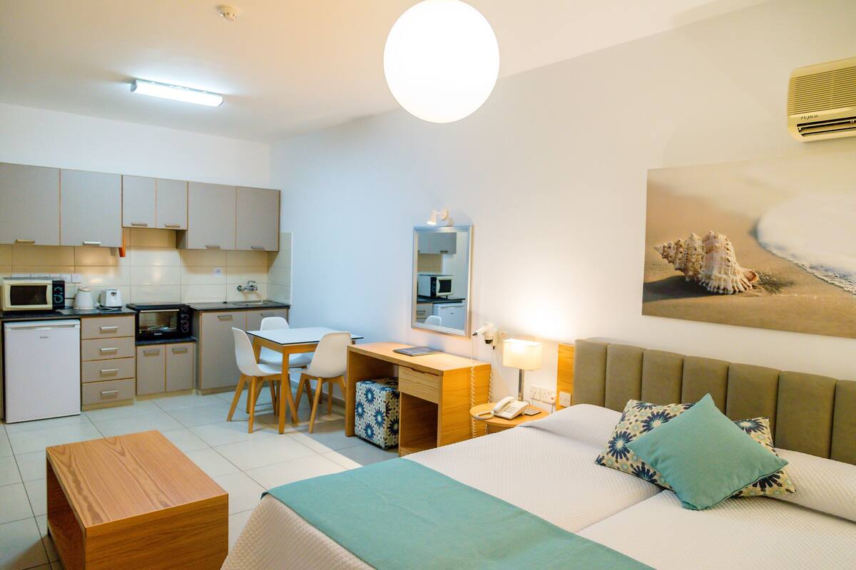 Une chambre d’hôtel comprenant un lit, un bureau, une chaise, une petite kitchenette et une salle de bain.