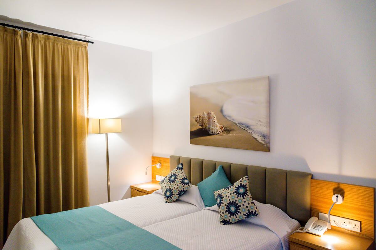 Une chambre d’hôtel avec un lit, deux oreillers, une table de chevet avec une lampe et un tableau au mur.