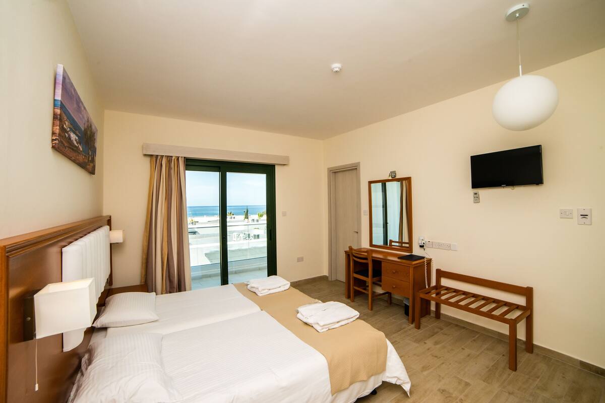 Une chambre d’hôtel avec un grand lit, un bureau, une chaise, une télévision et une vue sur la plage.