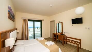A hotel room with a large bed, a desk, a chair, a TV, and a view of the beach.