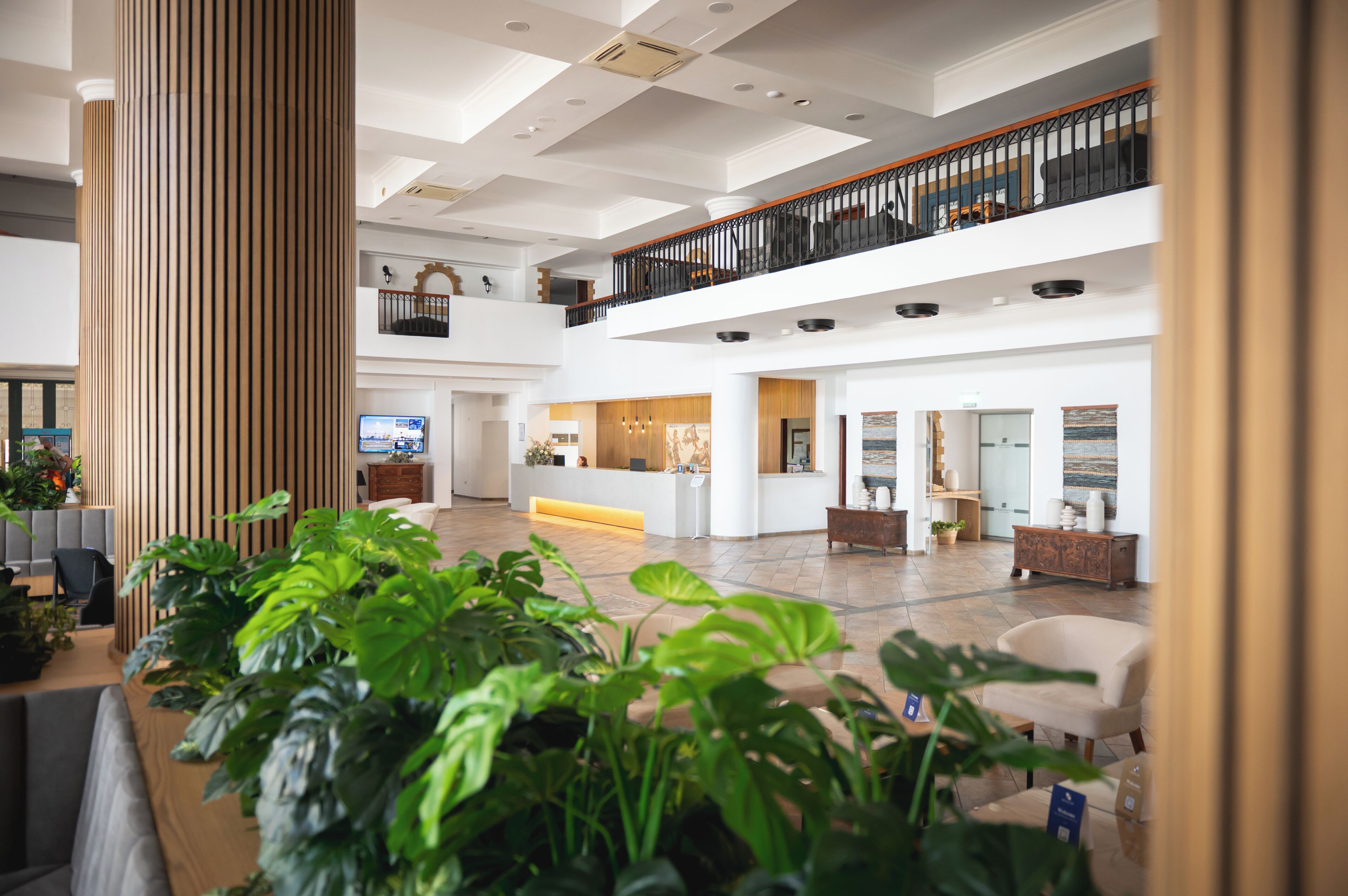 Eine geräumige Lobby mit hoher Decke, einer Holzsäule, einem Empfangstresen und einer Sitzecke.