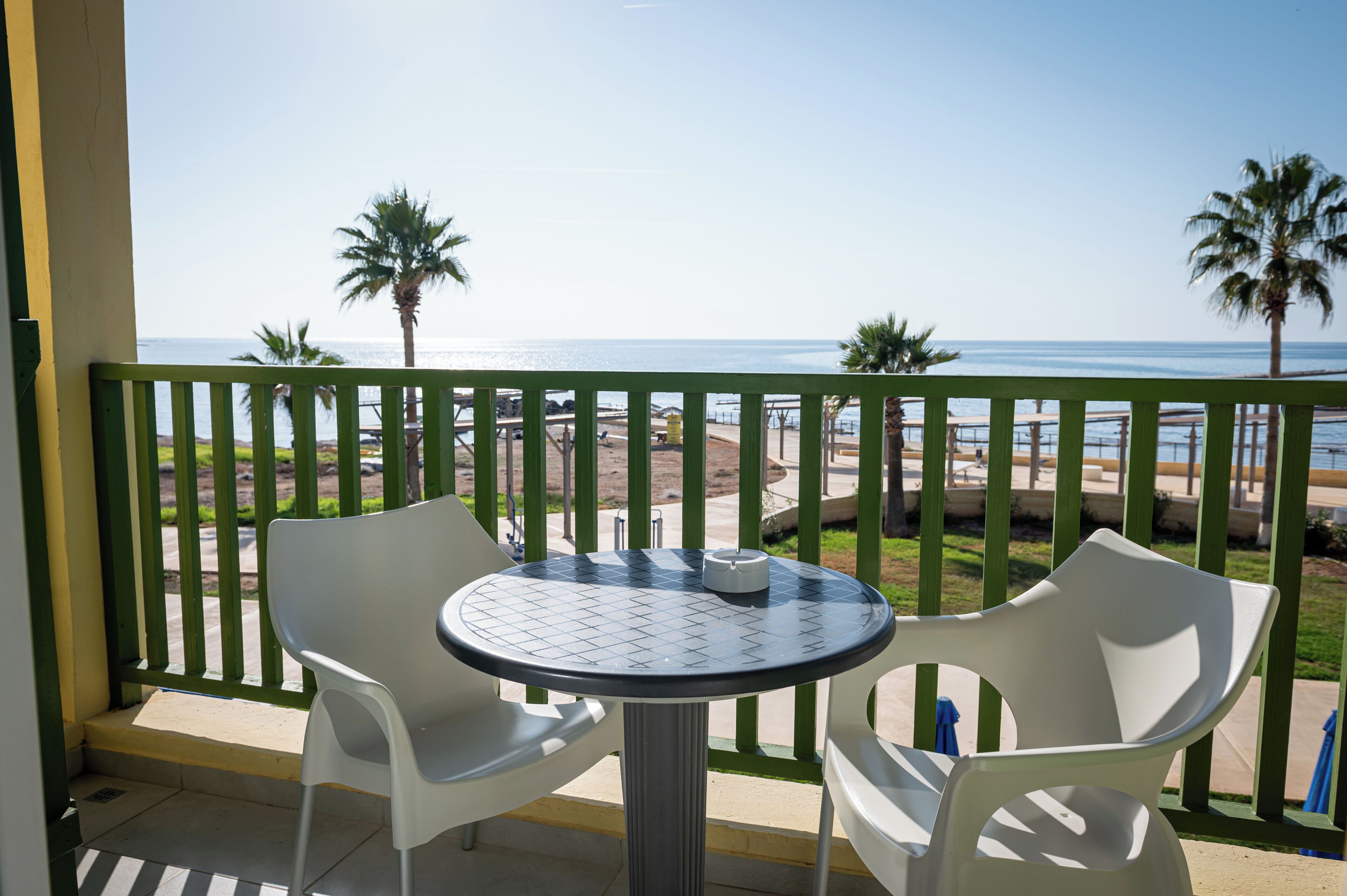 A balcony with a table and chairs, overlooking a beach with palm trees and the ocean.