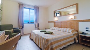 Habitación de hotel con cama, silla, escritorio, espejo y ventana con cortinas.
