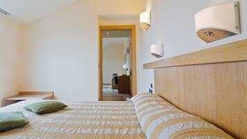 Une chambre d’hôtel avec un lit, une tête de lit en bois, une table de chevet et une lampe fixée au mur.