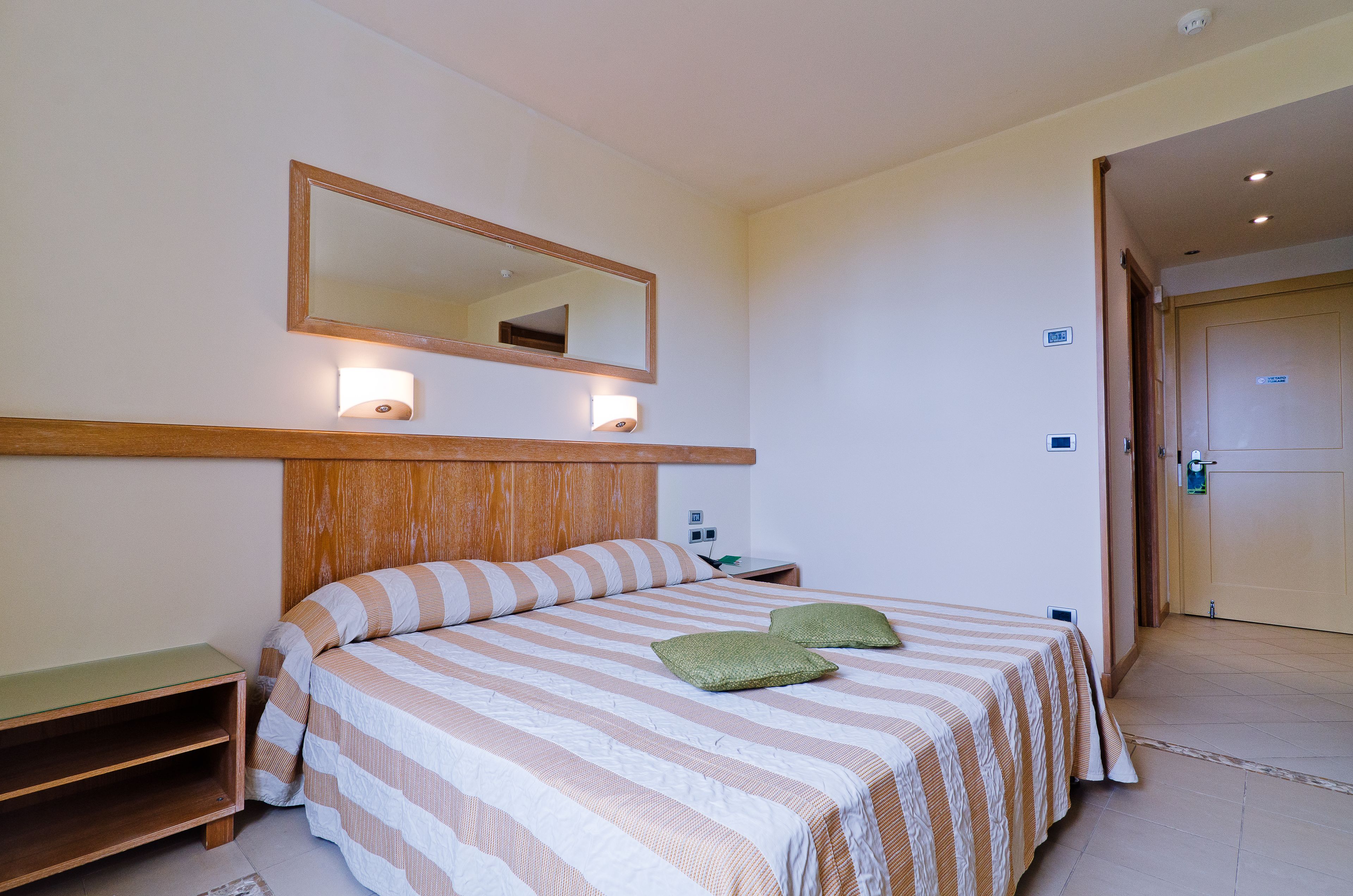 Una camera d'albergo con un letto, un comodino, uno specchio e una porta.