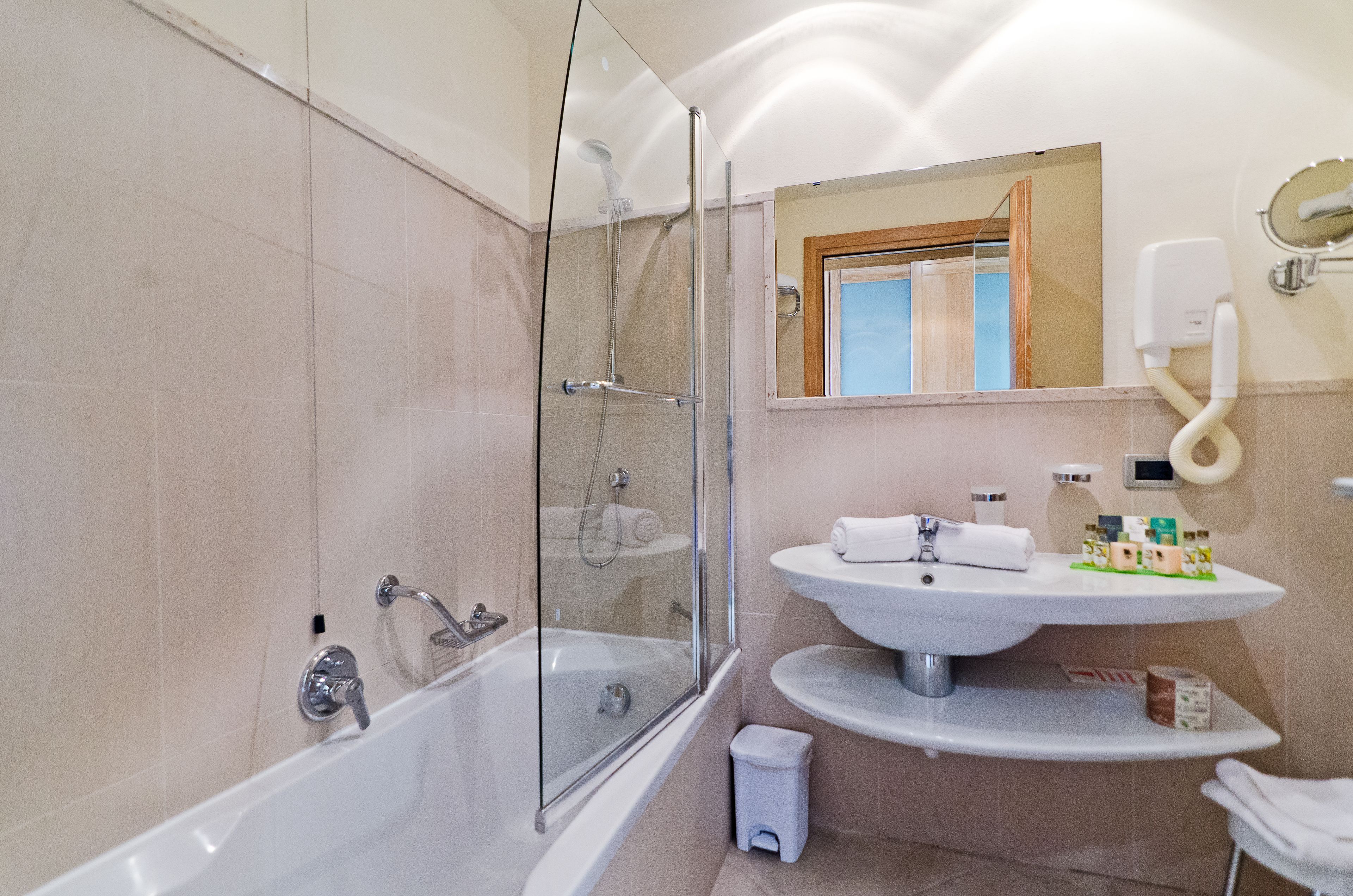 Un baño moderno con ducha envuelta en vidrio, un lavamanos blanco con un espejo encima y un pequeño cesto de basura.