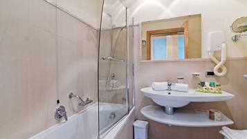 Un baño moderno con ducha envuelta en vidrio, un lavamanos blanco con un espejo encima y un pequeño cesto de basura.
