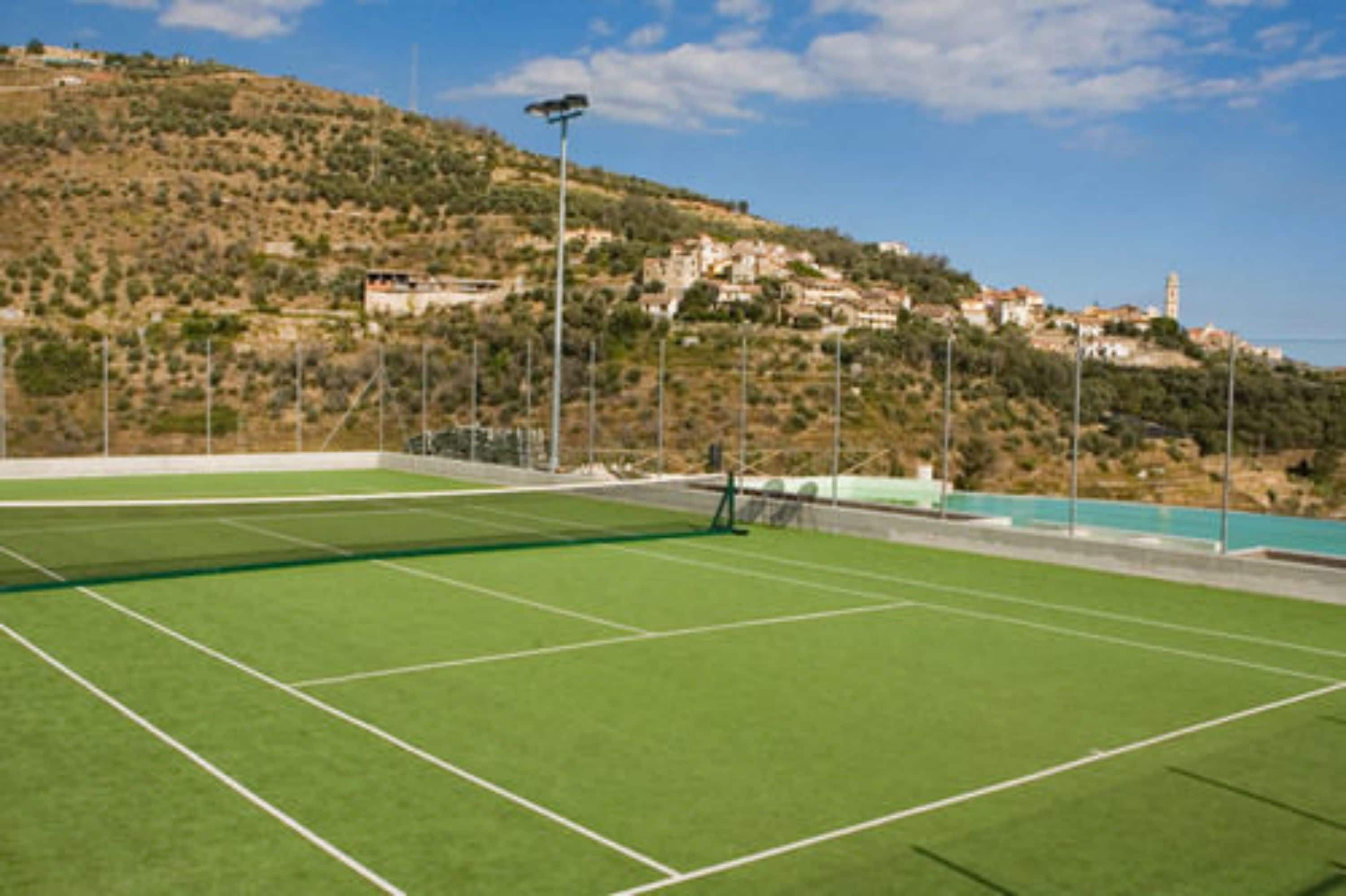 A tennis court with a clear view of a hillside with buildings and a tower in the background.