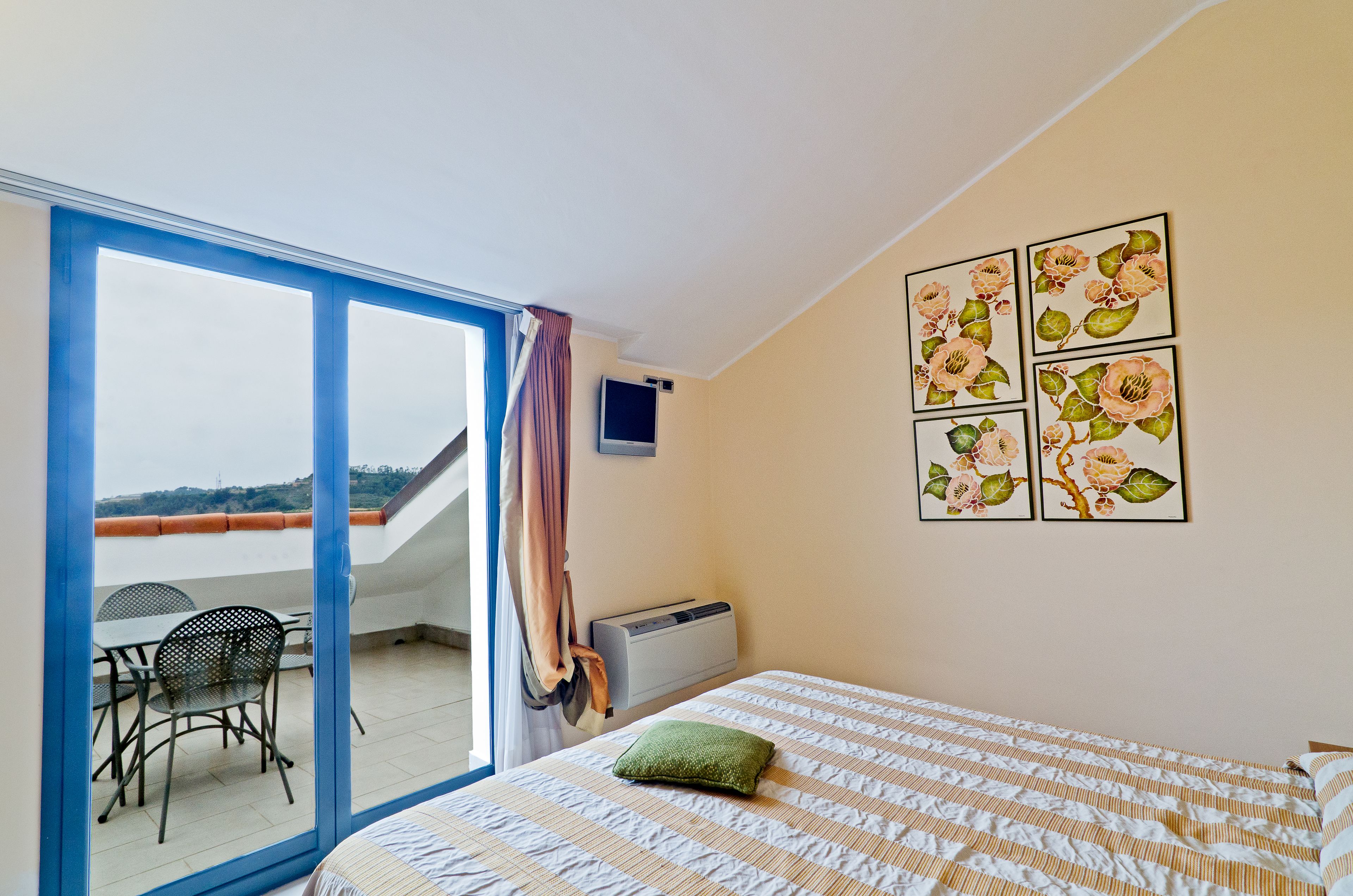 Ein Schlafzimmer mit einem Bett, einem grünen Kopfkissen, einem Fernseher und einer Wand mit floraler Dekoration.