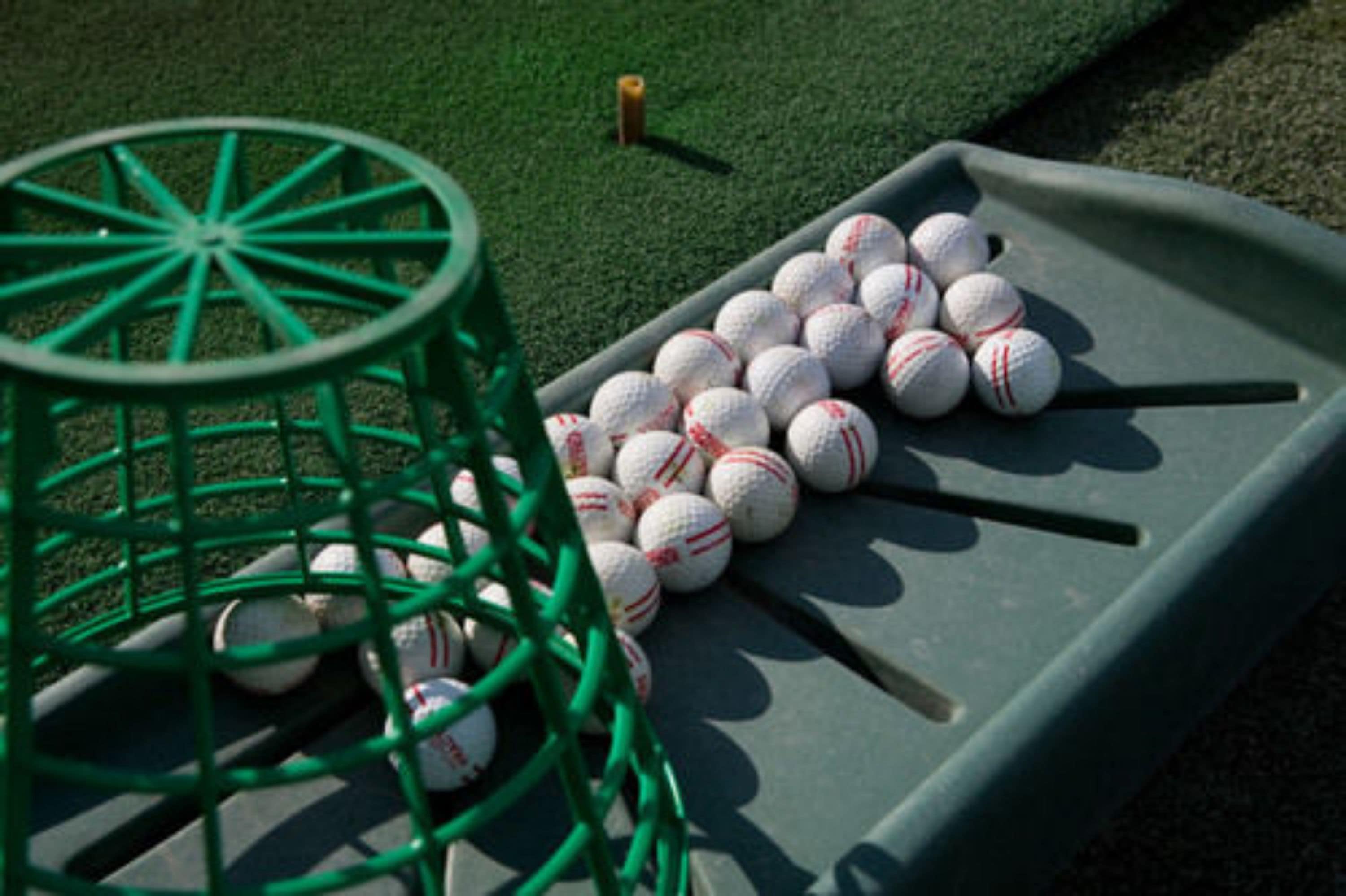 Un panier vert rempli de balles de golf, posé sur une surface verte.