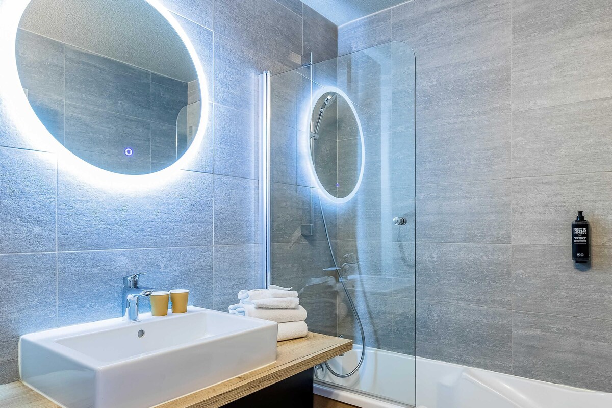 A modern bathroom with a large mirror, a sink, and a glass-enclosed shower.