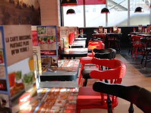 A restaurant interior with red chairs, tables, and menu boards. - ibis Styles Crolles Grenoble A41 (Crolles)