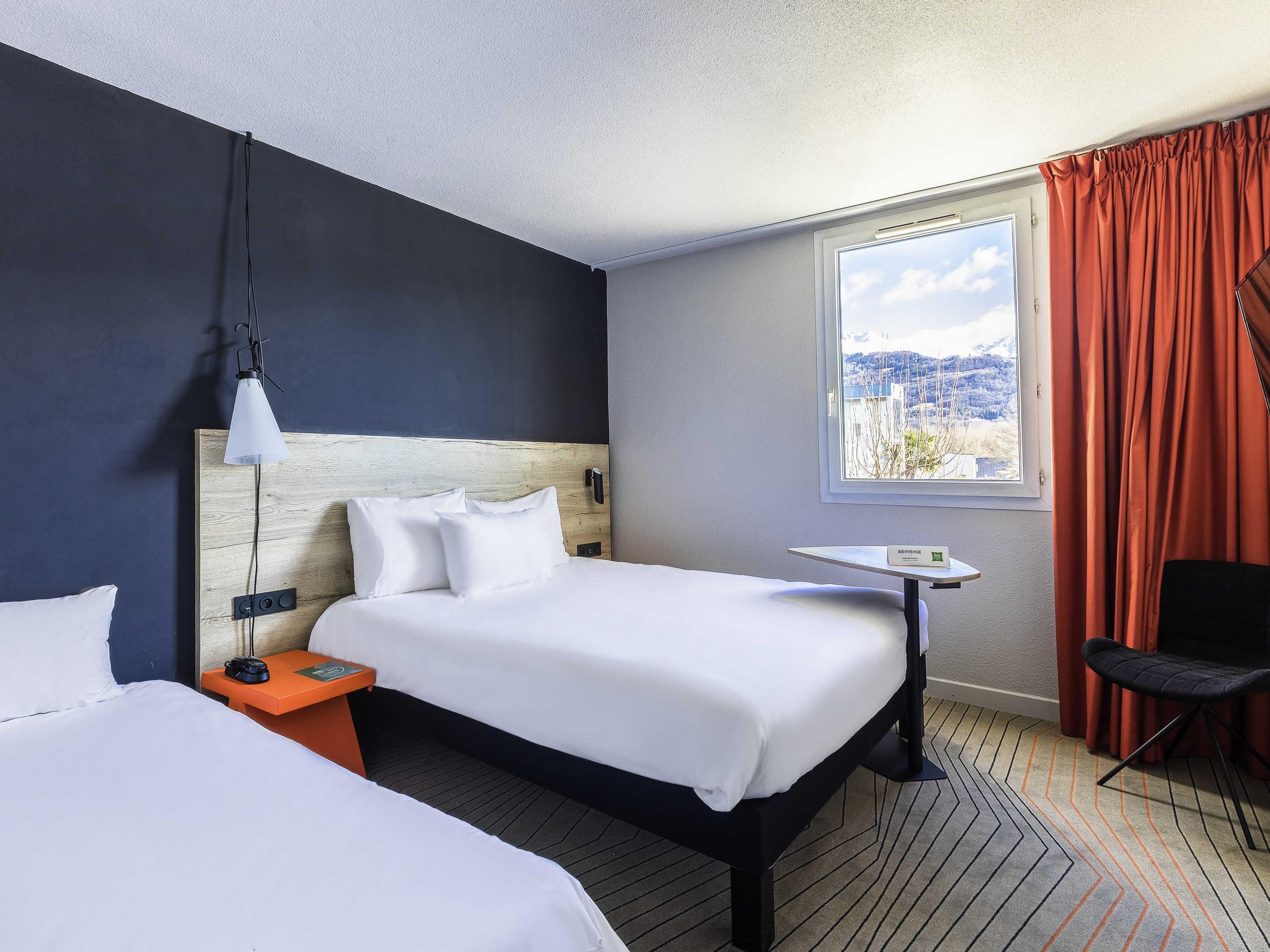 A hotel room with a large bed, a bedside table, a chair, a window with curtains, and a view of a snowy landscape.