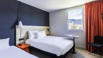 A hotel room with a large bed, a bedside table, a chair, a window with curtains, and a view of a snowy landscape.