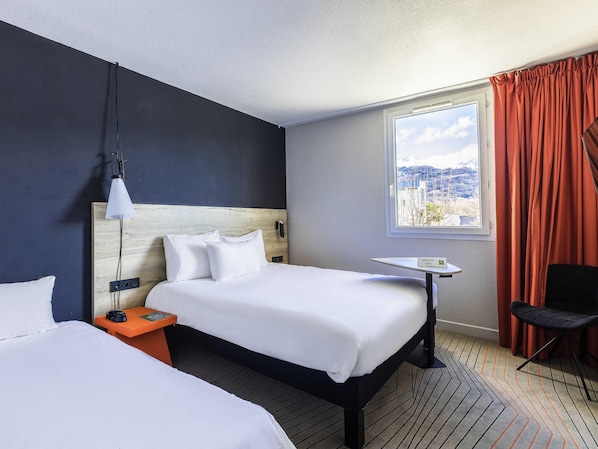 Habitación de hotel con una cama grande, una mesita de noche, una silla, una ventana con cortinas y vistas a un paisaje nevado.