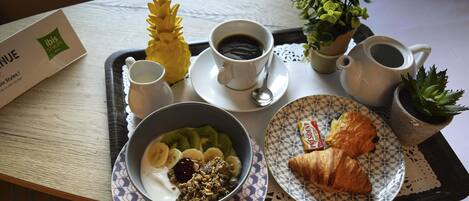 Uma bandeja com itens de café da manhã, incluindo uma tigela de iogurte com frutas, um croissant, um pequeno pastel e duas xícaras de café.