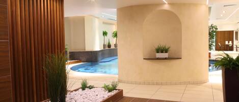 Un área de piscina interior moderna con una pared de madera, una zona de estar con una jardinera y vistas a la piscina.