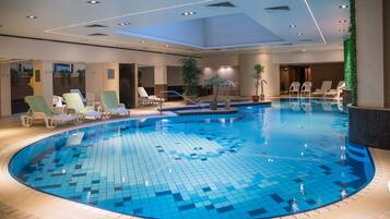 Una grande piscina interna con poltrona relax e piante in vaso lungo il bordo.