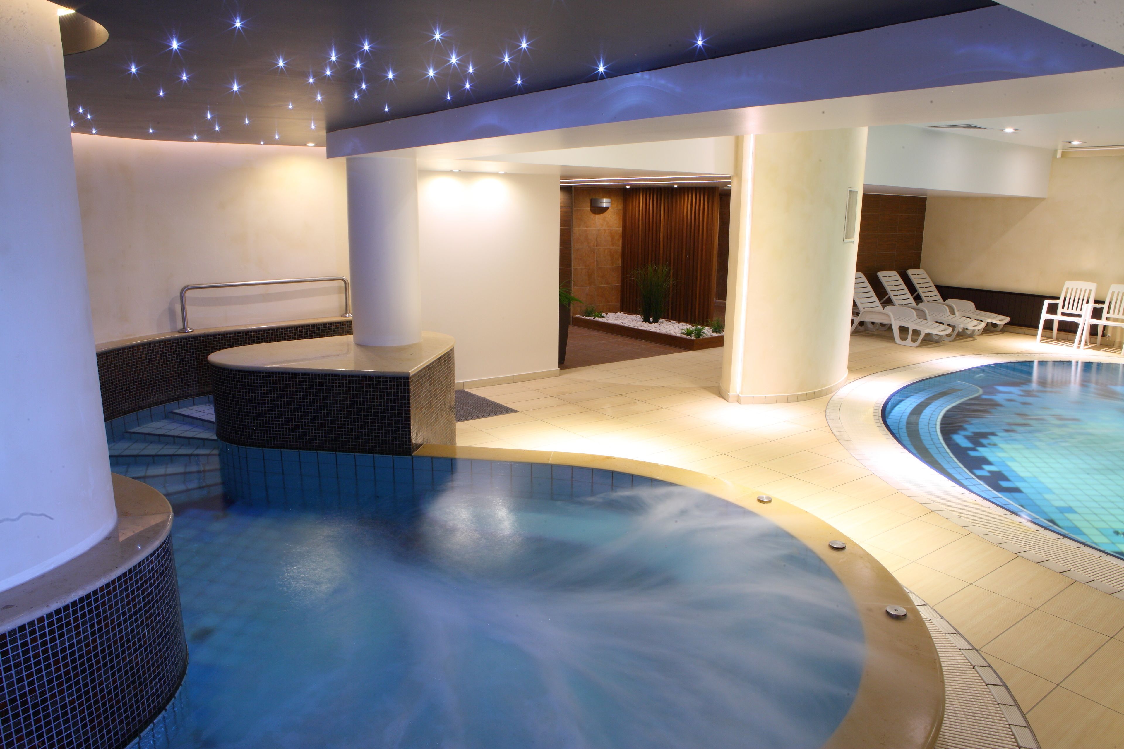 Un área de spa con un jacuzzi, sillones reclinables y una piscina.