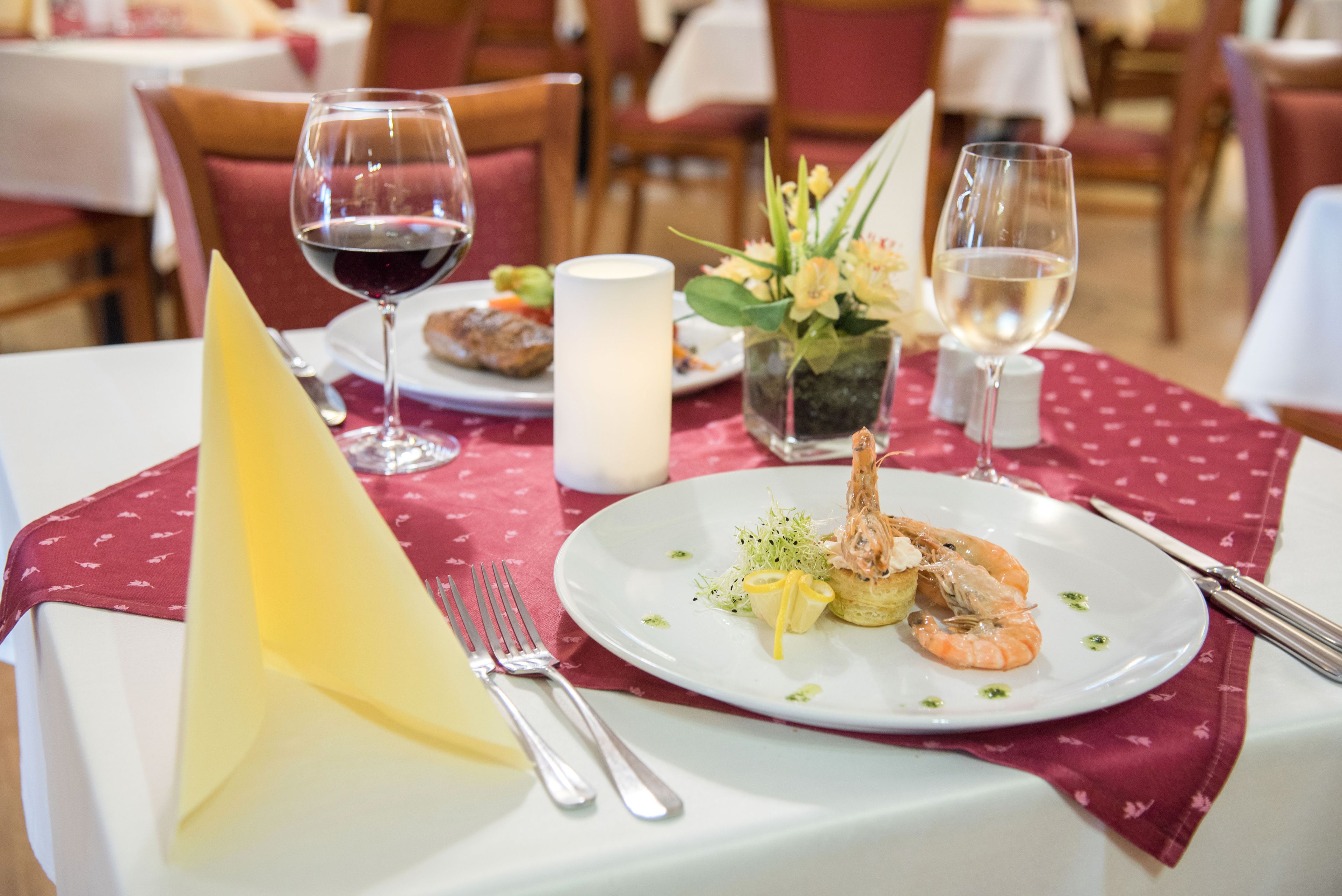 Une table à manger avec une assiette blanche remplie de fruits de mer, un verre de vin rouge et une bougie.