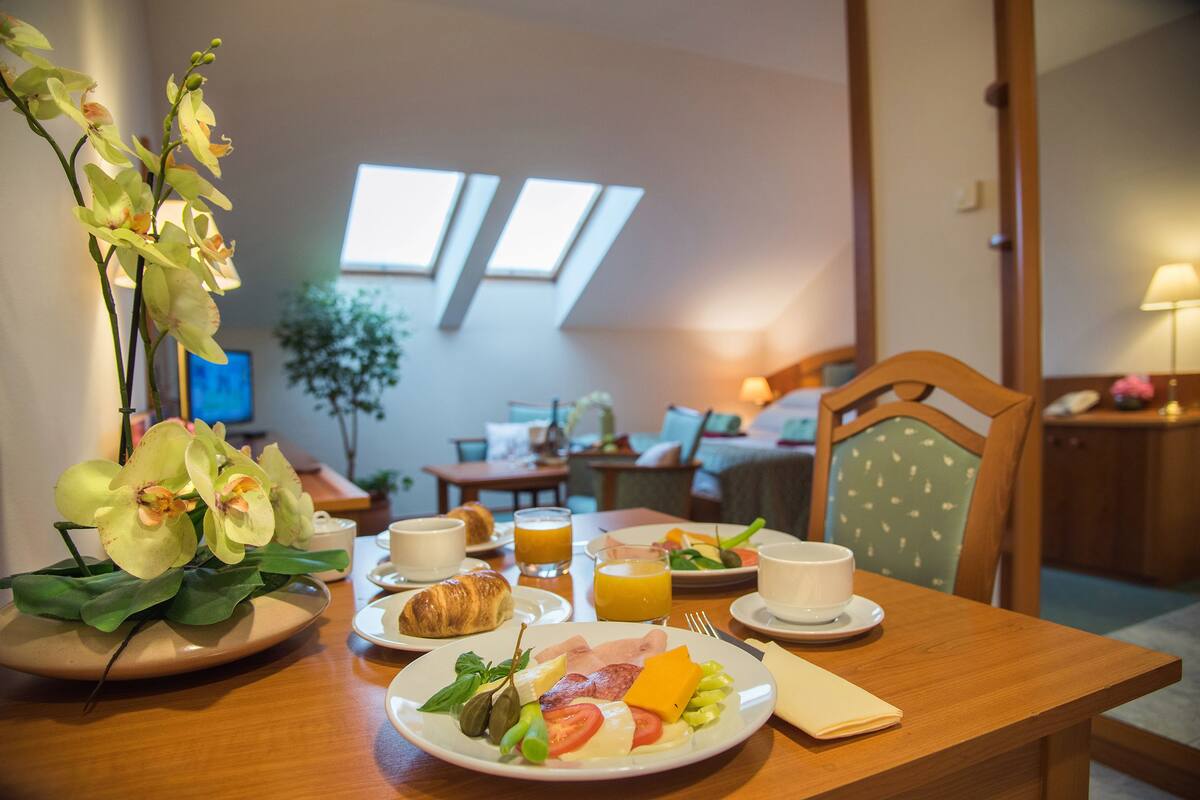 A breakfast table with plates of food, a croissant, and a vase of orchids.