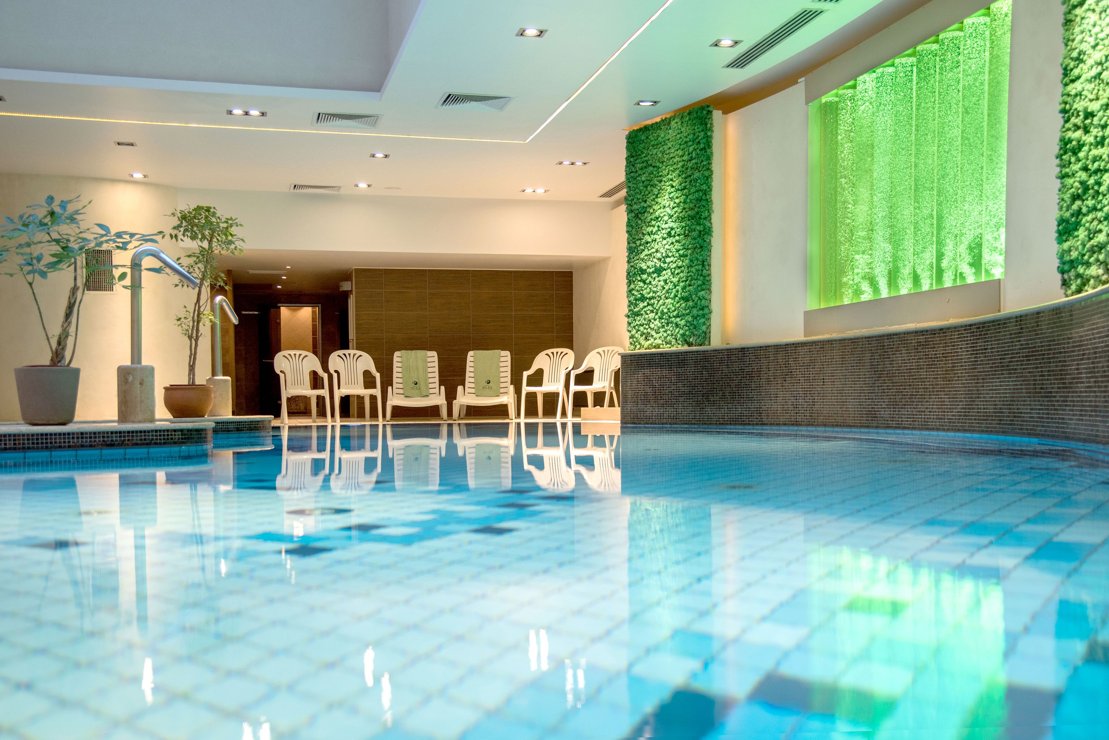 A swimming pool with clear blue tiles, white chairs along the edge, and green vertical gardens on the walls.