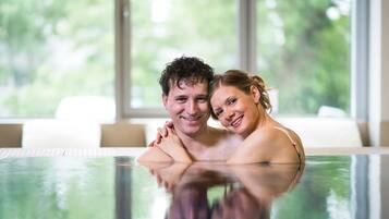 A couple in a hot tub with a view of greenery outside.