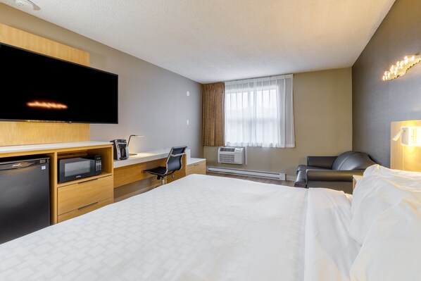 Habitación de hotel con cama, escritorio con silla, televisor, microondas y aire acondicionado.