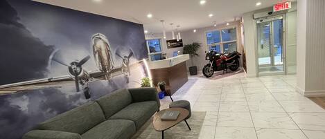 Un vestíbulo moderno con un mural grande de un avión, un mostrador de recepción, una motocicleta y un área de descanso.
