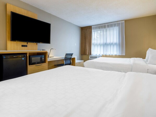 Habitación de hotel con dos camas, televisión, escritorio con silla, minibar y ventana con cortinas.