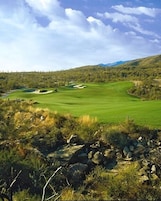 Un campo de golf con cielo despejado, colinas onduladas y algunos árboles.