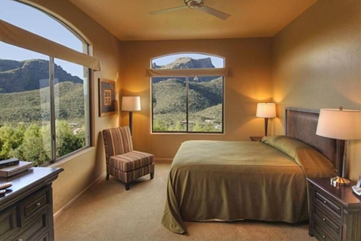 A bedroom with a large window, a bed, a chair, and a desk.