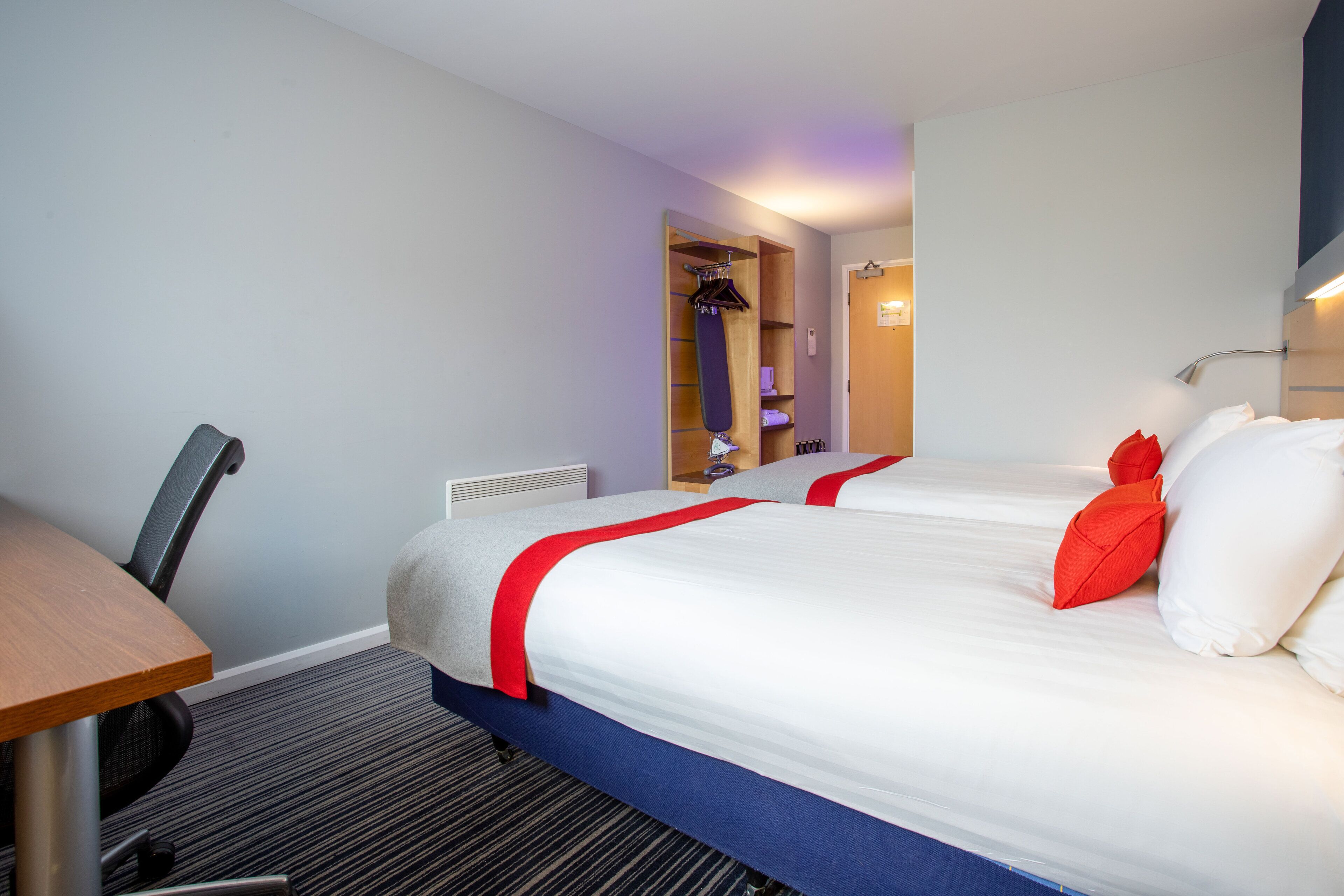 A hotel room with two beds, a desk, and a chair.