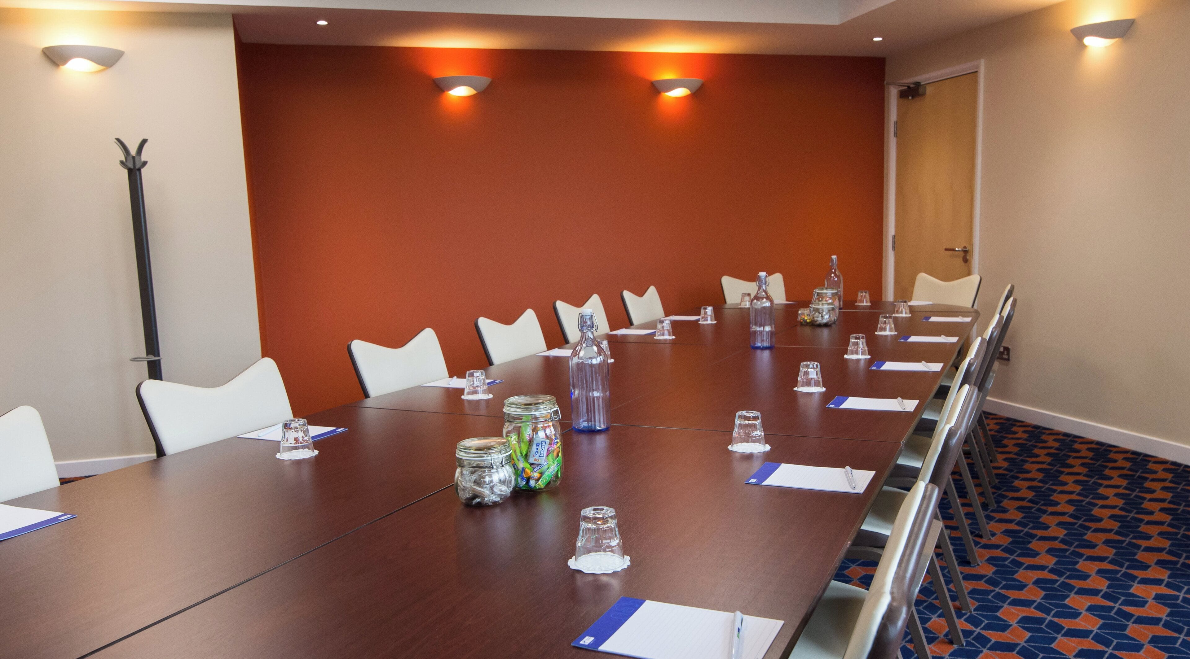 Ein Konferenzraum mit einem langen Tisch, weißen Stühlen und einer roten Akzentwand.