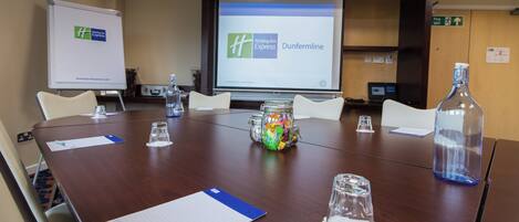A conference room with a large table, chairs, a projector screen, and a whiteboard.