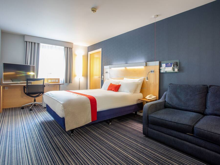 A hotel room with a bed, a desk, a television, a sofa, and a mirror.
