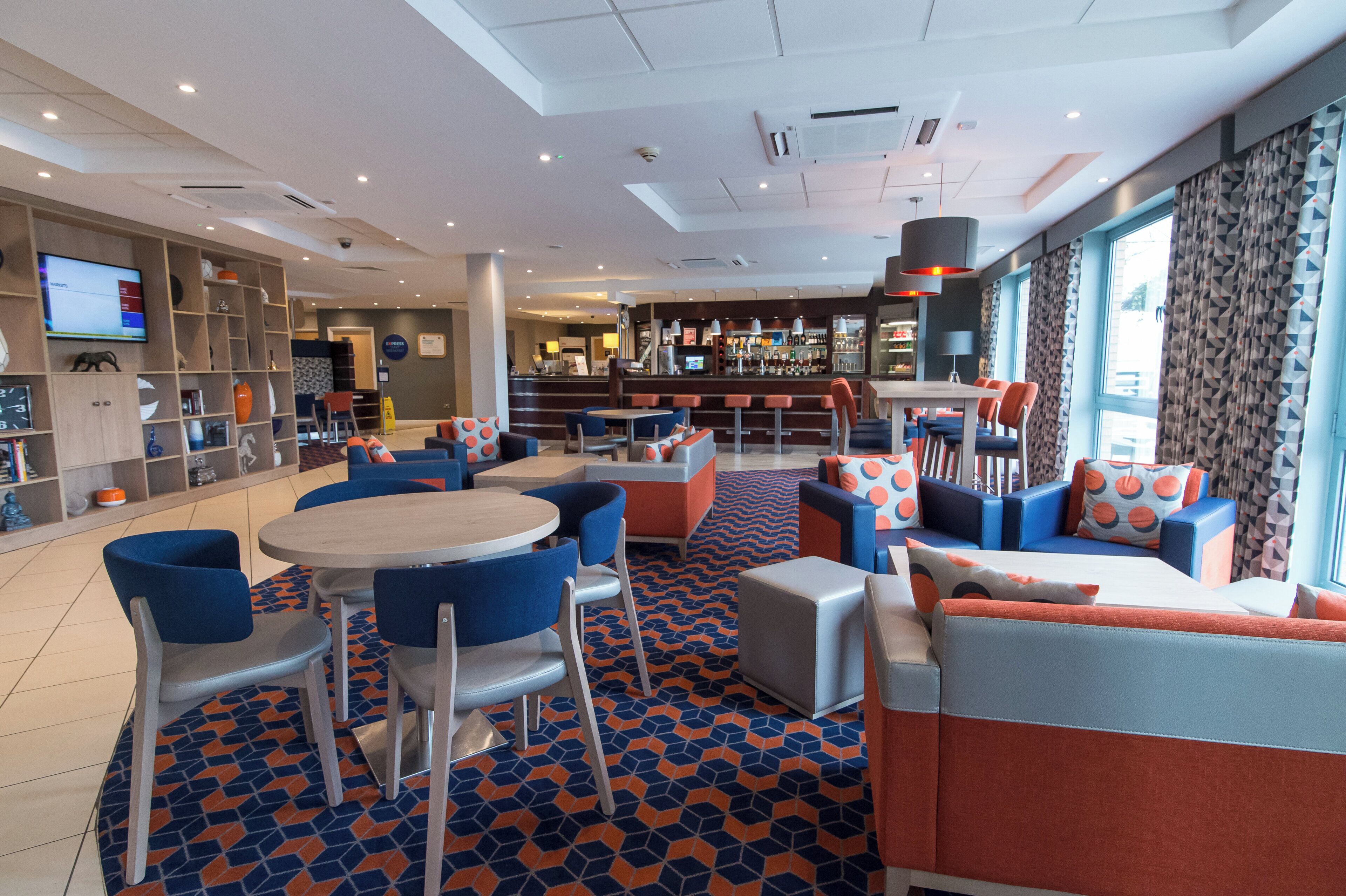 Un hall d’hôtel moderne doté d’un bar, d’espaces aménagés avec des sièges et d’un écran de télévision.