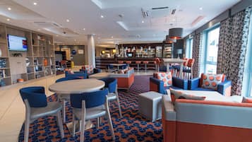 Eine moderne Hotelhalle mit Barbereich, Sitzgelegenheiten und einem Fernsehbildschirm.