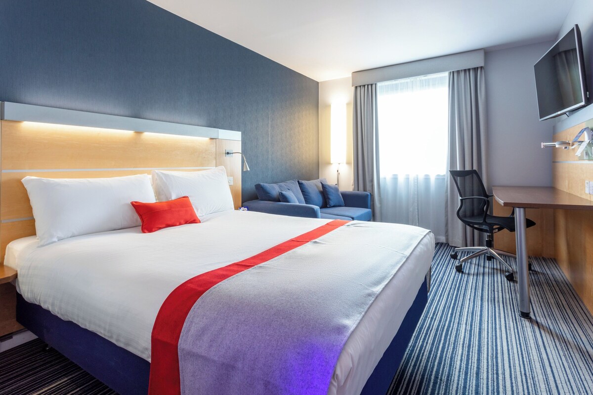 Una habitación de hotel con una cama grande, un escritorio, una silla y un televisor.