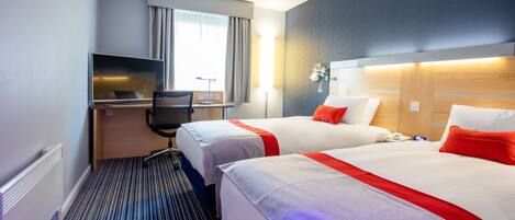 Quarto de hotel com duas camas, uma escrivaninha, televisão e janela com cortinas.