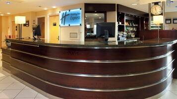 Un espace d’accueil d’hôtel avec un comptoir d’accueil incurvé, une horloge numérique et une enseigne Holiday Inn Express.