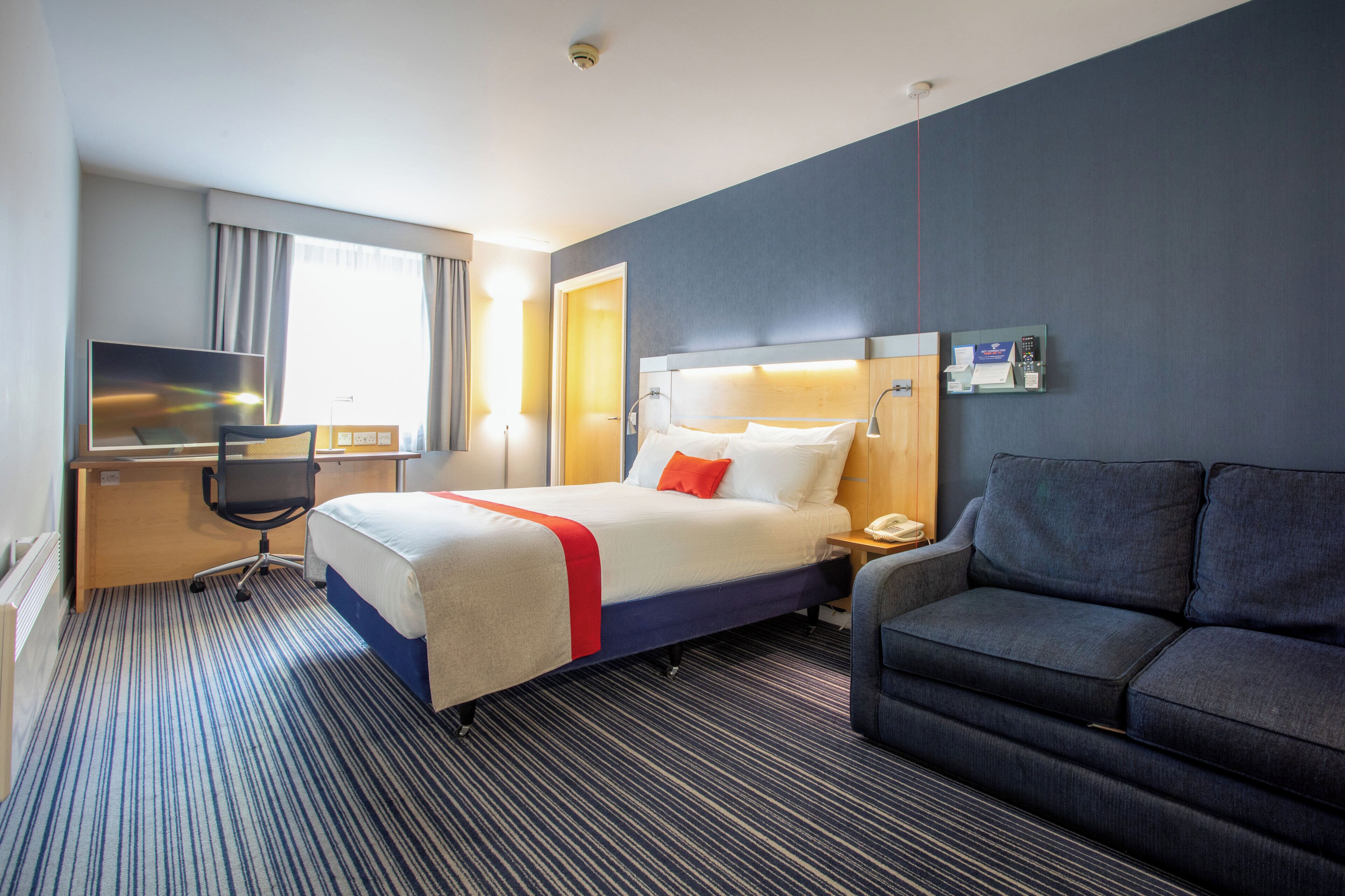 A hotel room with a bed, a desk, a chair, a couch, and a television.
