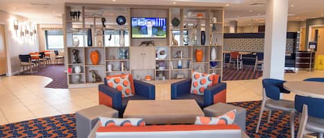 A hotel lobby with seating, a television, and a variety of decorative items on shelves.
