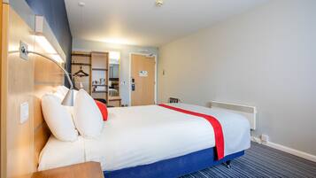A hotel room with a large bed, a bedside table, a lamp, a heater, and a wardrobe.