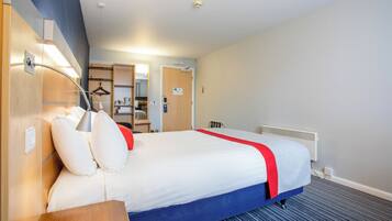 A hotel room with a bed, bedside table, lamp, and a radiator.