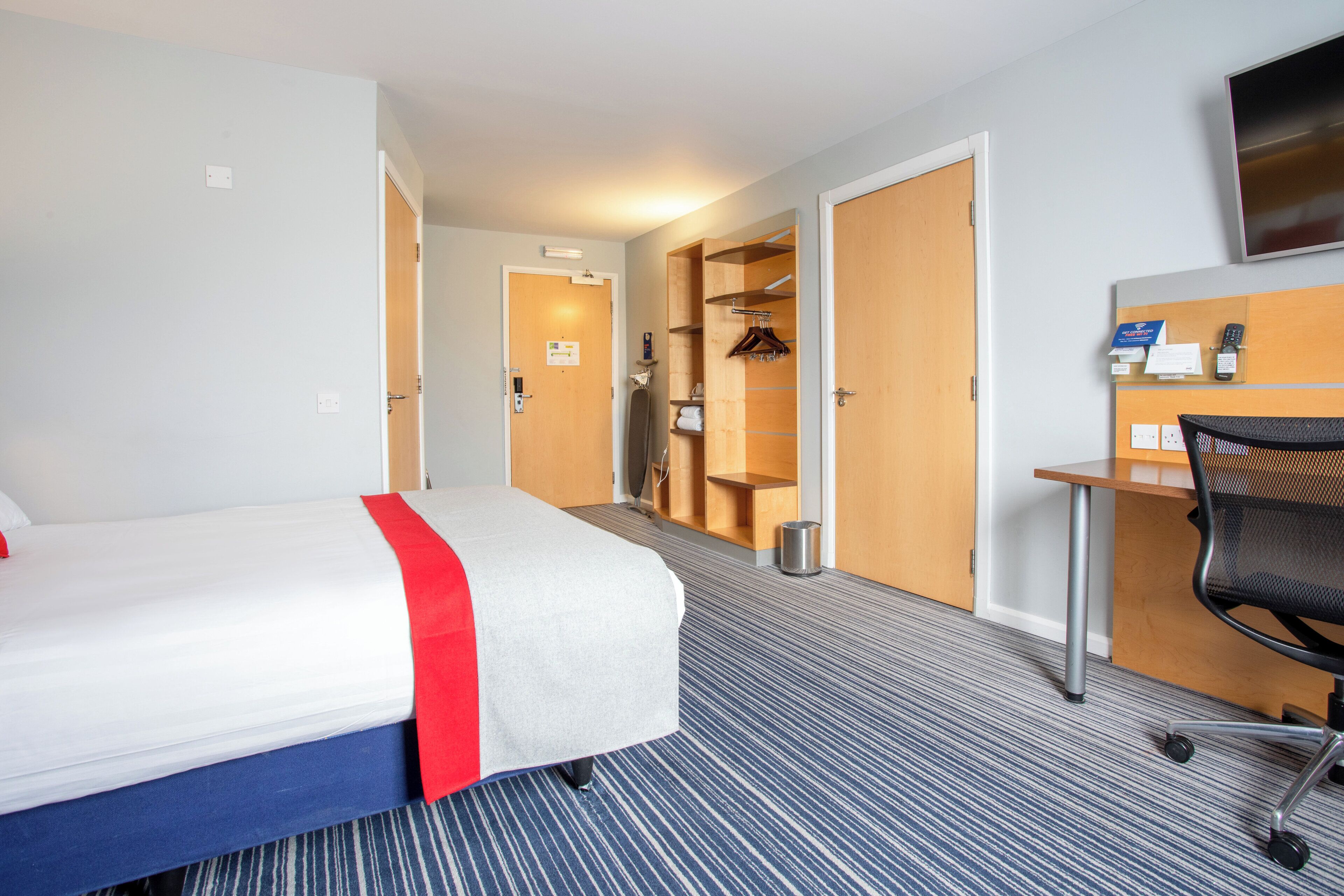 Habitación de hotel con cama, escritorio, silla, televisor y baño visible a través de una puerta abierta.