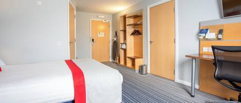 Habitación de hotel con cama, escritorio, silla, televisor y baño visible a través de una puerta abierta.