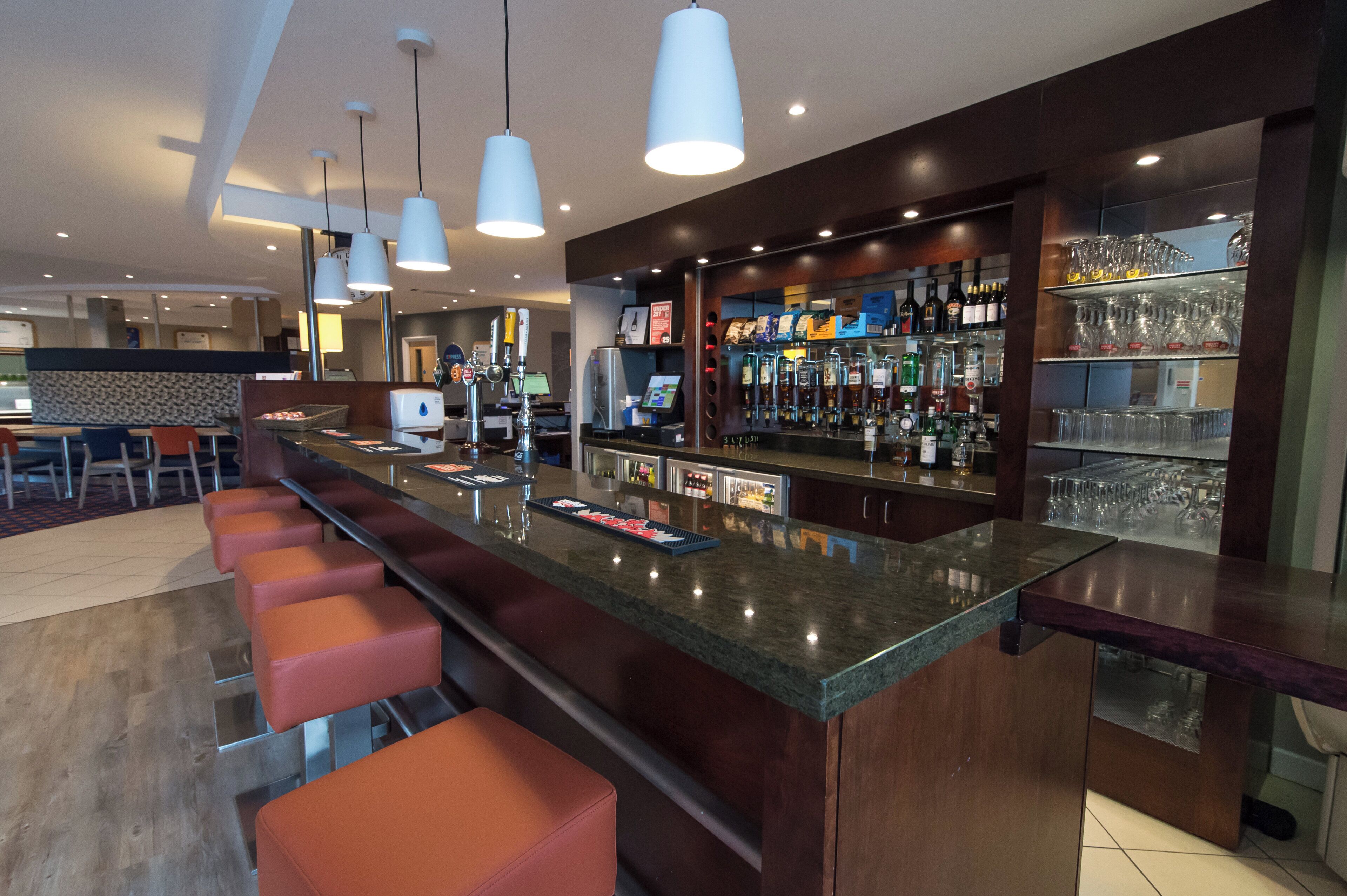 Zona de bar moderna con una barra larga, múltiples grifos y una selección de botellas y vasos.