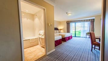 A hotel room with a large bed, a separate bathroom, a seating area with a chair, and a view of the outdoors through a sliding door.